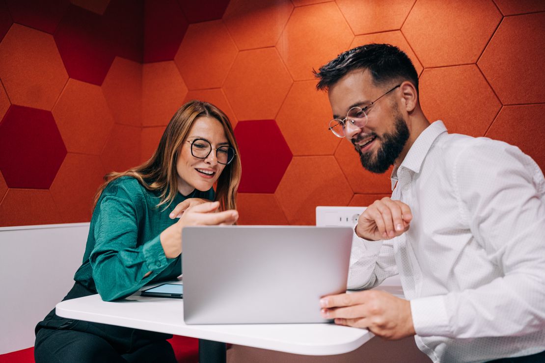 Une femme et un homme assis à une table regardent un ordinateur portable, semblant collaborer.