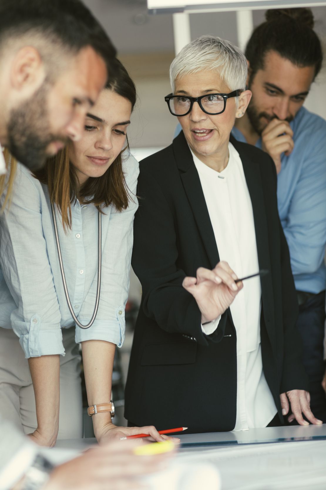 Quatre collègues sont réunis autour d’une table ; une femme en blazer désigne avec un stylo tout en menant la discussion.