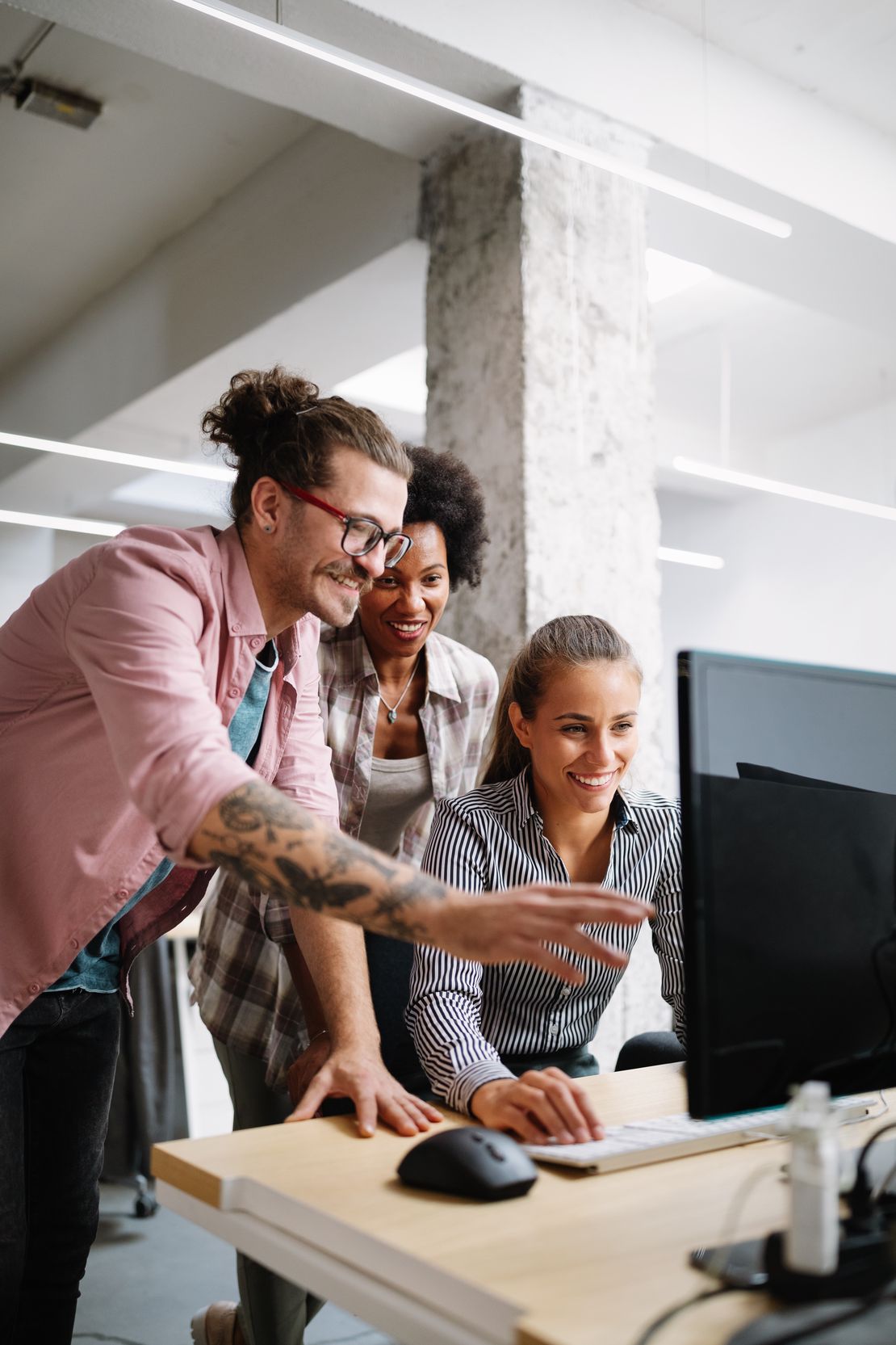 Trois collègues sourient en regardant un écran d’ordinateur ; l’un pointe du doigt tandis que les autres observent de près.